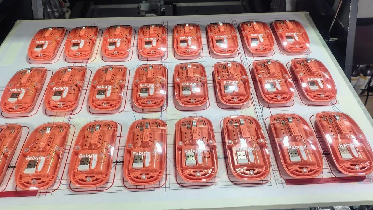 A batch of orange computer mice laid out on the UV flatbed for logo printing